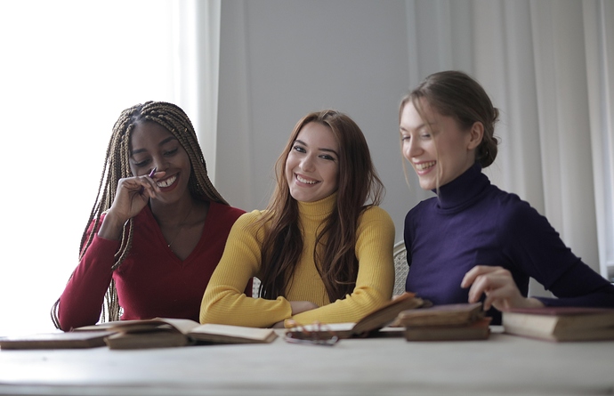 cheerful-young-women-sitting-at-table-with-books-and-talking-3884172
