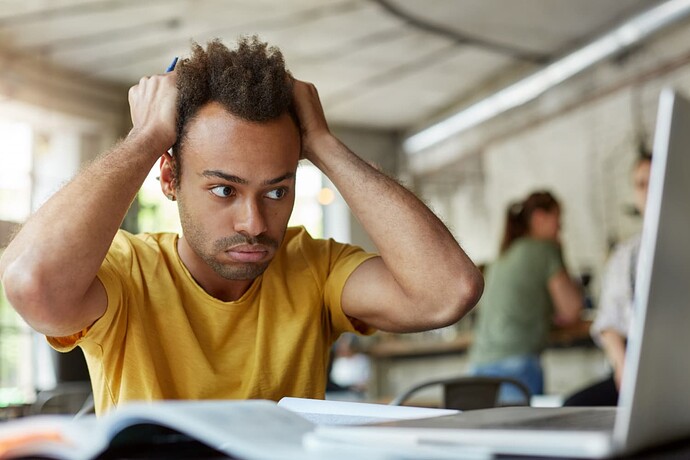 stressed-young-african-american-student-feeling-frustrated-sitting-coworking-space-front-open-laptop-computer-holding-head-with-hands
